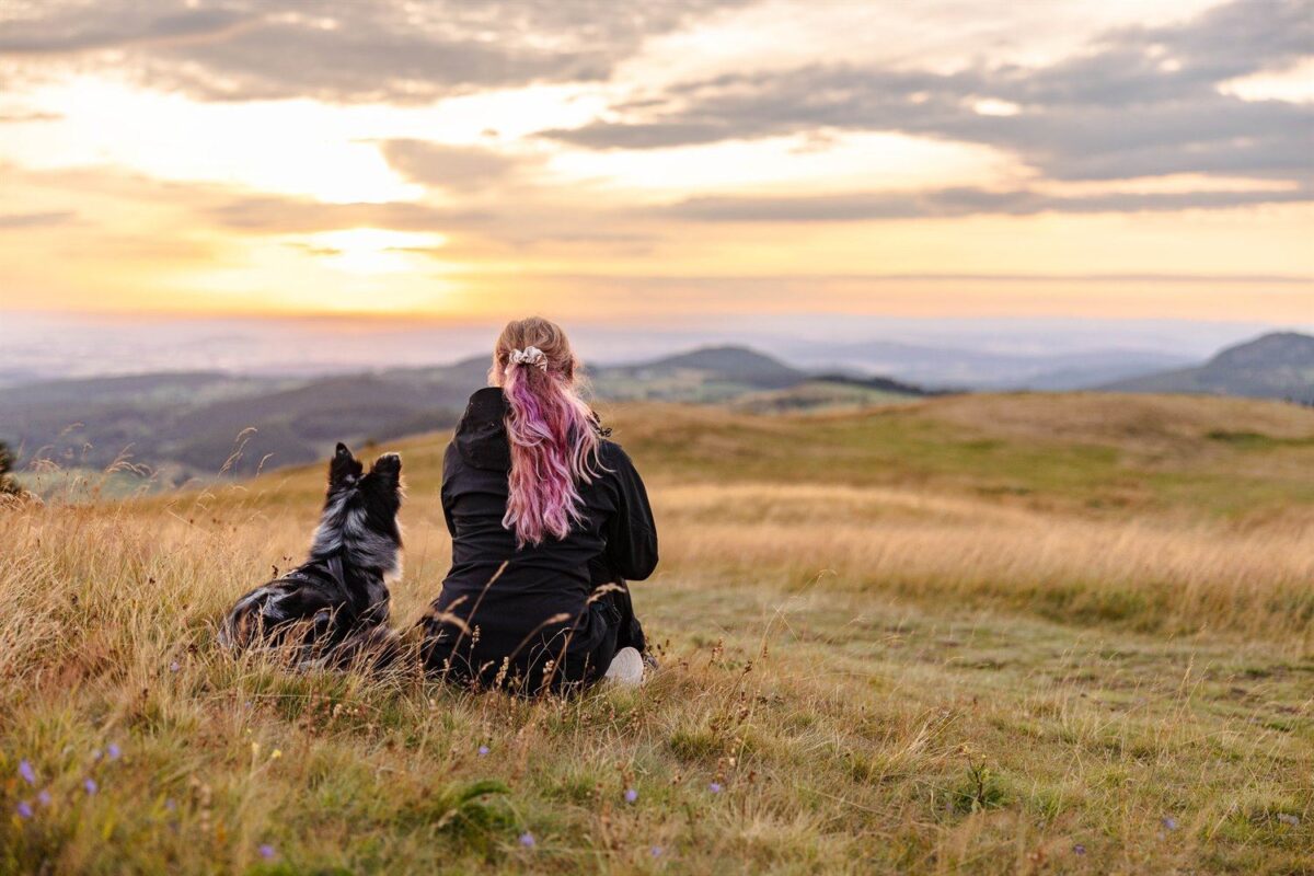 Mensch und Hund genießen den Sonnenuntergang auf der Wasserkuppe während eines Hundefotoshootings in der Rhön